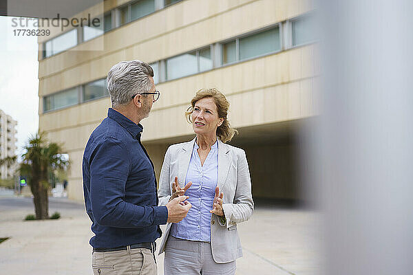 Geschäftsfrau diskutiert mit Geschäftsmann vor Bürogebäude