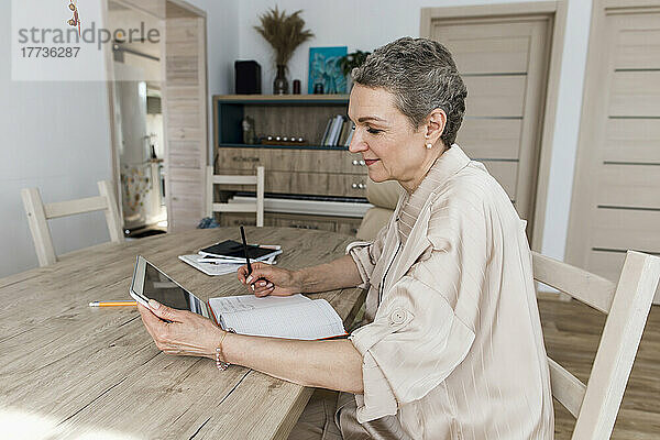 Frau nutzt digitales Tablet und macht sich zu Hause am Tisch Notizen