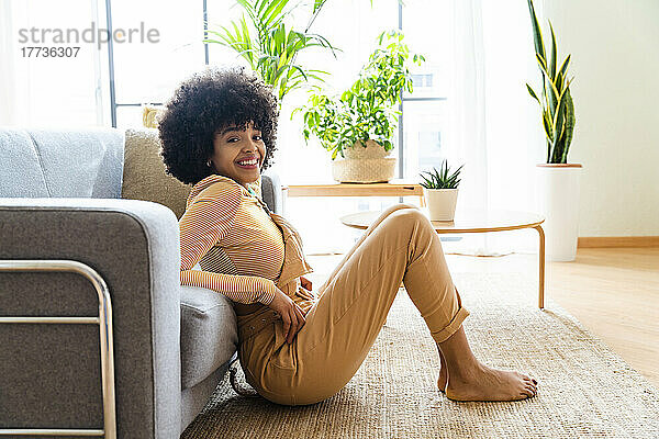 Lächelnde Afro-Frau lehnt zu Hause auf dem Sofa