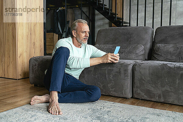 Reifer Mann benutzt Mobiltelefon und sitzt zu Hause auf dem Sofa