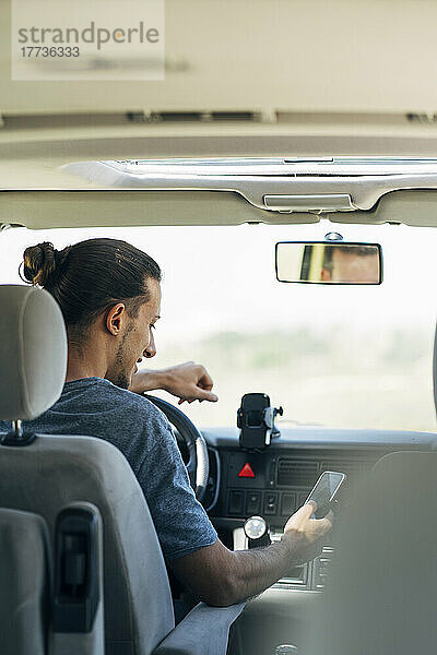 Junger Mann  der im Transporter sitzt und Textnachrichten über sein Smartphone sendet