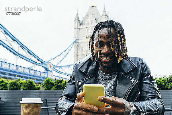 Lächelnder Mann  der Textnachrichten auf dem Smartphone sendet  London  England