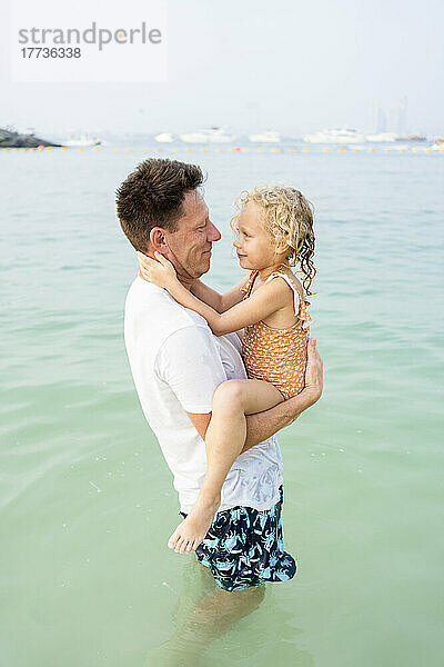 Lächelnder Vater trägt seine Tochter im Wasser am Strand
