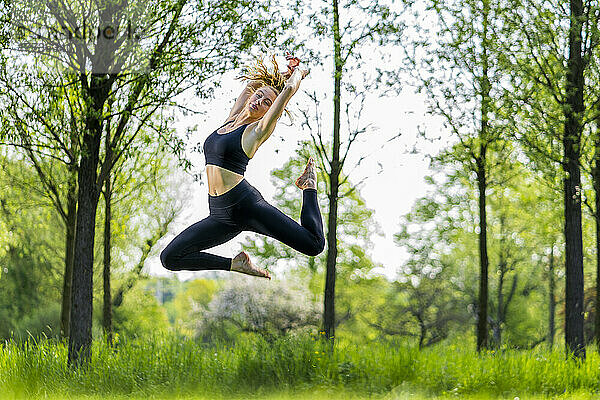 Junge Frau springt über Wiese im Park