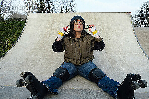 Frau mit Rollschuhen sitzt auf Rampe im Skatepark