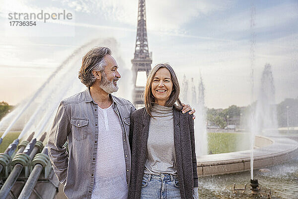Glücklicher reifer Mann mit Arm um Frau  der vor dem Eiffelturm  Paris  Frankreich steht