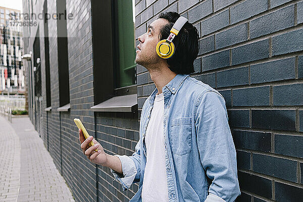Mann mit Kopfhörern schaut nach oben und hält ein Smartphone in der Nähe der Wand