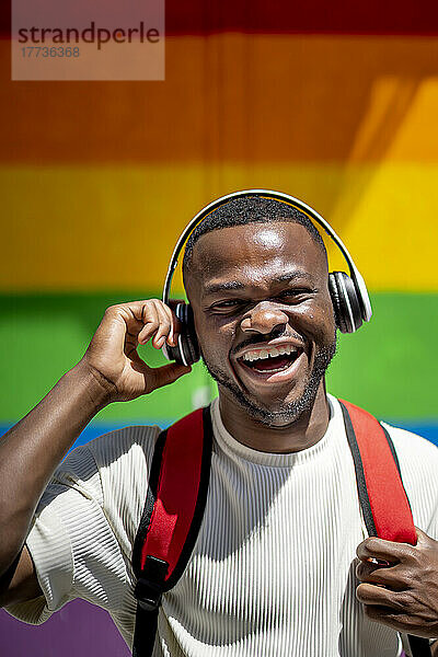 Glücklicher Mann mit kabellosen Kopfhörern vor der Regenbogenwand