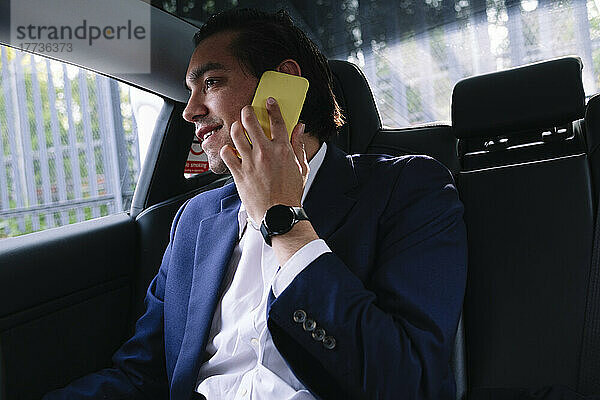 Lächelnder Geschäftsmann  der im Elektroauto sitzt und auf dem Smartphone spricht