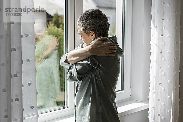 Reife Frau steht zu Hause am Fenster