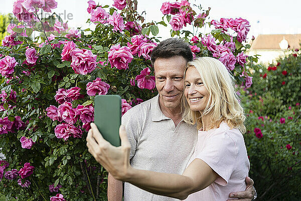 Lächelndes Paar macht Selfie im Rosengarten