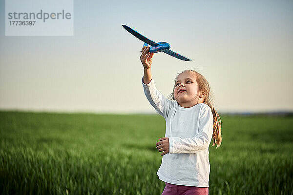 Verspieltes Mädchen fliegt Spielzeugflugzeug auf dem Feld bei Sonnenuntergang