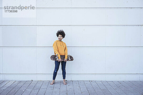 Junge Frau hält Skateboard und steht vor der Wand