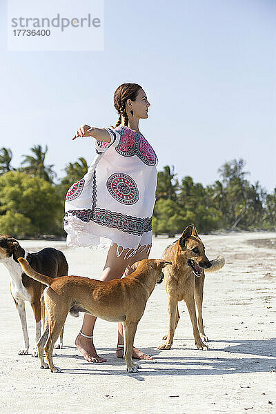 Frau mit ausgestreckten Armen steht neben Hunden am Strand