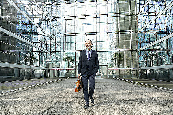 Geschäftsmann mit Tasche läuft vor modernem Glasgebäude