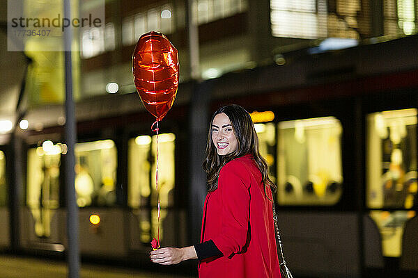 Glückliche Frau hält nachts einen herzförmigen Ballon