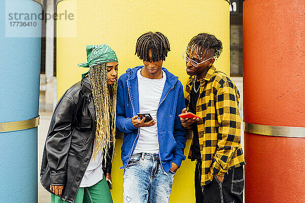 Junger Mann teilt Smartphone mit Freunden vor gelbem Rohr