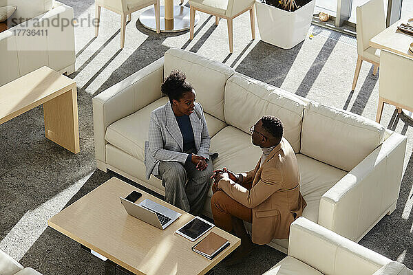 Junge Geschäftsfrau bespricht Plan mit Kollegin  die auf dem Sofa im modernen Büro sitzt