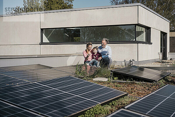 Glückliches Mädchen mit Eltern  die vor einem Solarpanel auf dem Dach sitzen