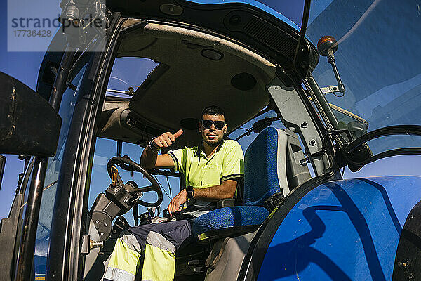 Bauer mit Sonnenbrille gestikuliert im Traktor und zeigt Daumen nach oben
