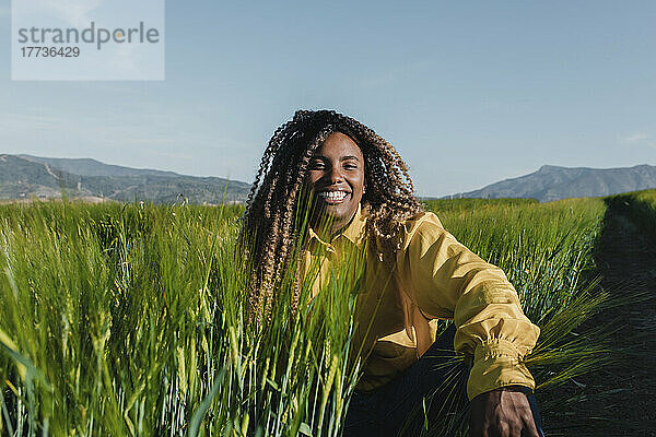 Glückliche Frau mit lockigem Haar  die an einem sonnigen Tag im Gras sitzt
