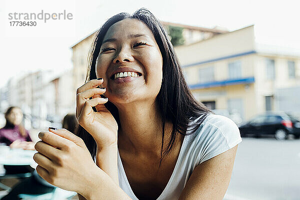 Cheerful young woman with eyes closed sitting at sidewalk cafe