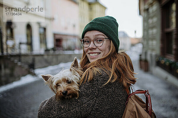 Glückliche rothaarige Frau mit Strickmütze und Yorkshire Terrier in der Stadt