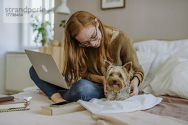 Glückliche Frau mit Brille streichelt Yorkshire Terrier zu Hause im Bett