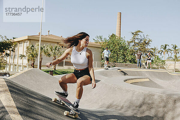 Junge Frau fährt Skateboard auf Sportrampe im Skatepark