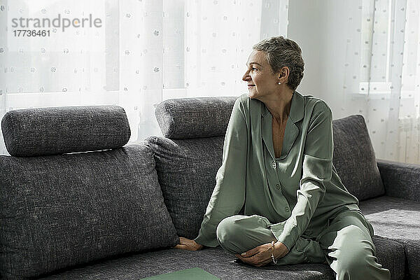 Mature woman sitting on couch in living room looking away