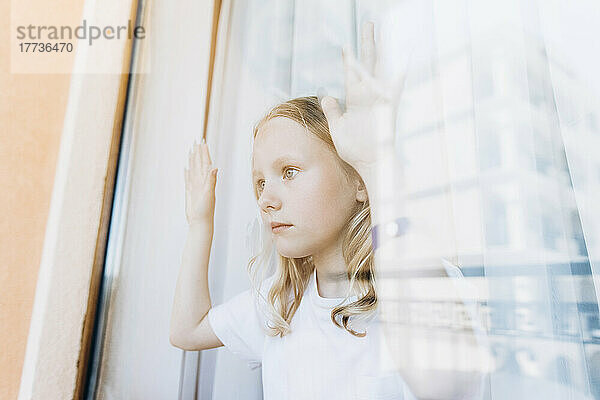 Nachdenkliches Mädchen  das zu Hause durch das Glasfenster schaut