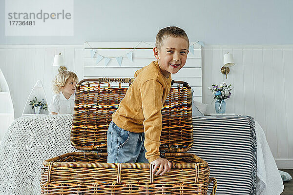 Happy boy standing in wicker basket by bed at home