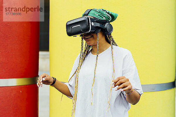 Glückliche Frau mit Virtual-Reality-Simulator  die vor einem gelben Betonrohr steht