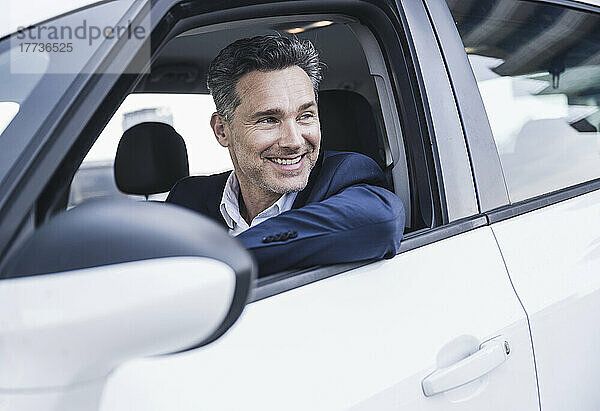 Lächelnder reifer Geschäftsmann sitzt im Auto