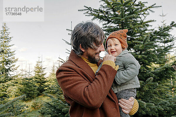 Glücklicher Vater trägt Sohn auf der Weihnachtsbaumfarm
