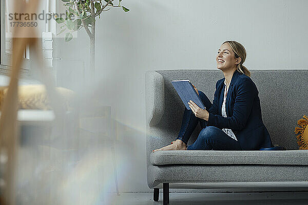 Lächelnde Geschäftsfrau mit Tablet-PC sitzt auf dem Sofa im Büro