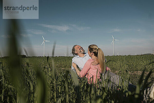 Glücklicher Mann mit Freundin  der an einem sonnigen Tag im Feld sitzt