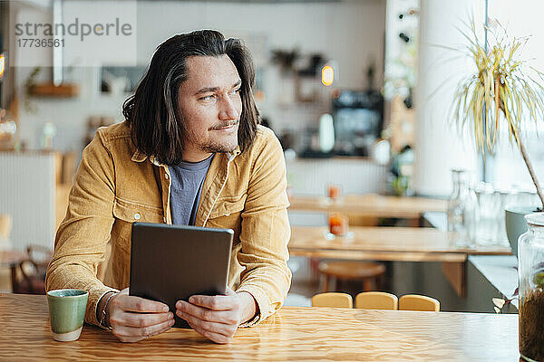 Lächelnder Hipster-Mann mit Tablet-PC sitzt am Tisch im Café