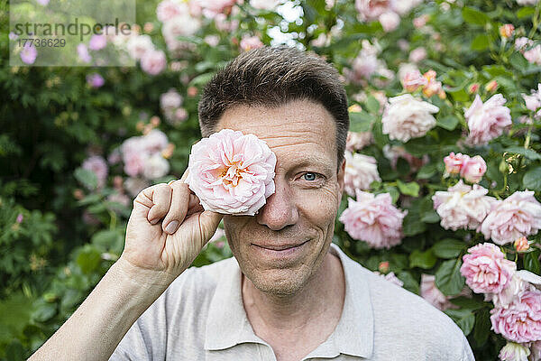 Smiling man holding rose in front of eye at garden