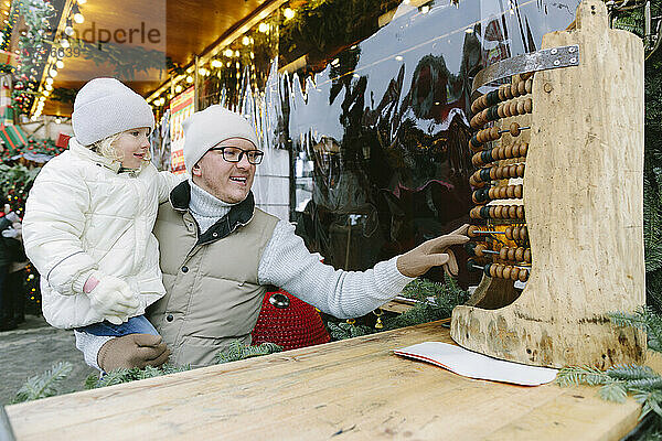 Vater und Tochter spielen mit Abakus auf dem Weihnachtsmarkt