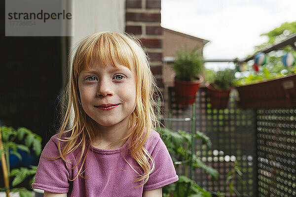 Lächelndes Mädchen mit roten Haaren sitzt auf dem Balkon