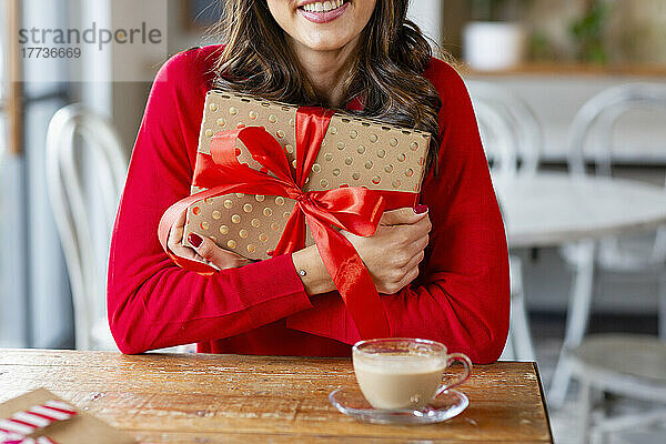 Glückliche Frau mit Weihnachtsgeschenk sitzt am Tisch im Café