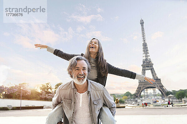 Glücklicher reifer Mann  der einer Frau Huckepackfahrt vor dem Eiffelturm  Paris  Frankreich  gibt
