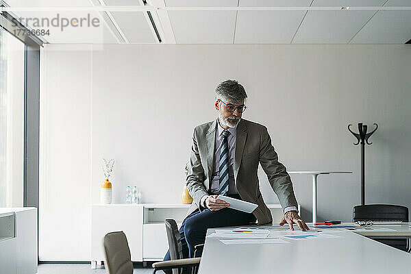 Geschäftsmann sitzt mit Tablet-PC und analysiert Dokumente auf dem Schreibtisch im Büro