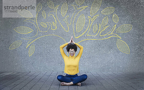 Glückliche junge Frau meditiert unter einem an die Wand gemalten Baum