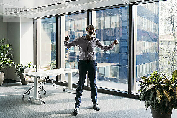 Geschäftsmann hört Musik über drahtlose Kopfhörer und tanzt vor dem Fenster im Büro