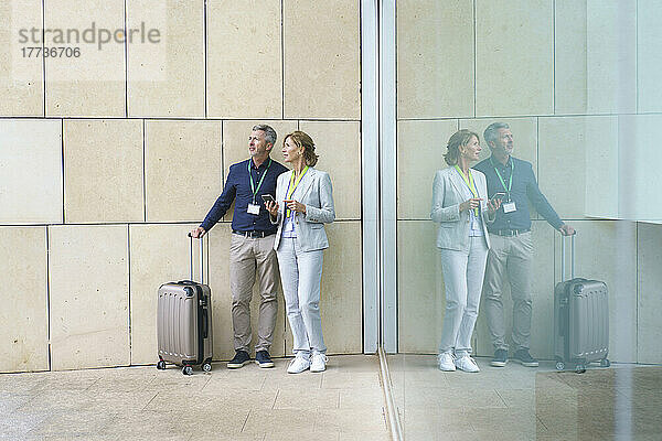 Geschäftsmann und Geschäftsfrau mit Koffer stehen an der Glaswand