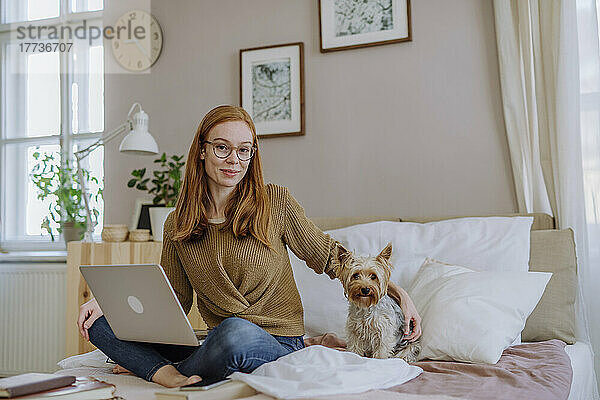 Lächelnde Frau mit Yorkshire Terrier sitzt zu Hause im Bett