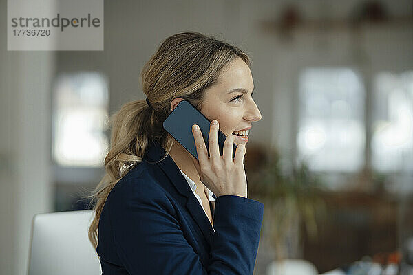 Glückliche Geschäftsfrau  die im Büro auf dem Smartphone spricht