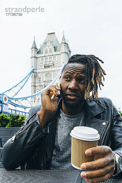 Junger Mann mit Einwegbecher spricht auf Smartphone  London  England